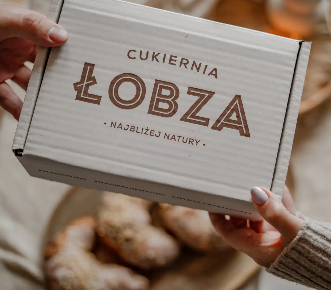 Karton z napisem Cukiernia Łobza podawany nad stołem z Rogalami Świętomarcińskimi
